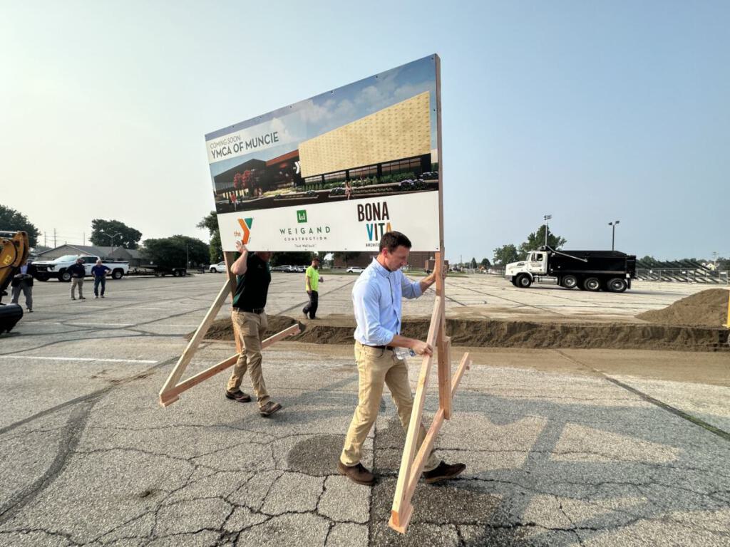 Neil (Project Manager) and Kreighton (Project Engineer) carry a sign with a rendering of the YMCA of Muncie.