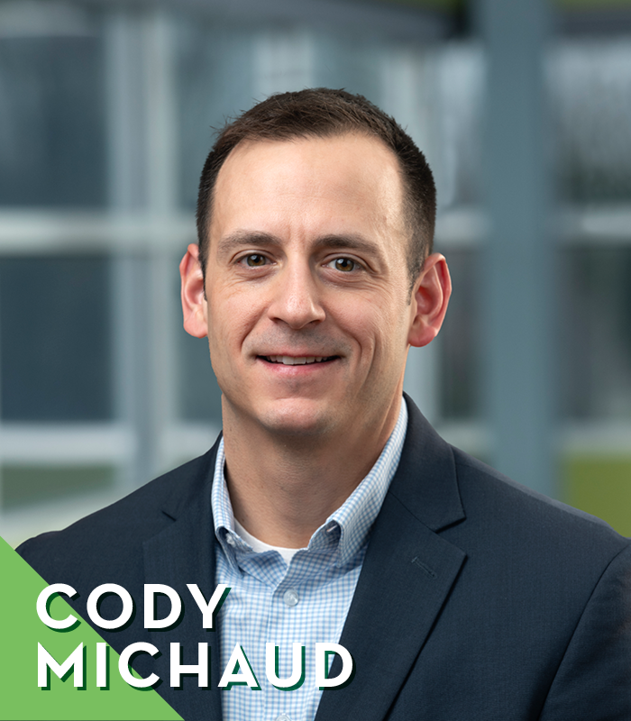 Feature Images Q2 2026 1 | Weigand Construction Portrait of Cody Michaud in a navy blazer, smiling, in a professional headshot for an About page (overlay text reads 'CODY MICHAUD').